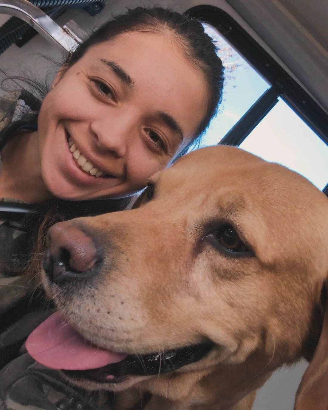 Dannielle Tyler smiling beside a yellow Labrador inside the Dirty Paws mobile grooming unit.