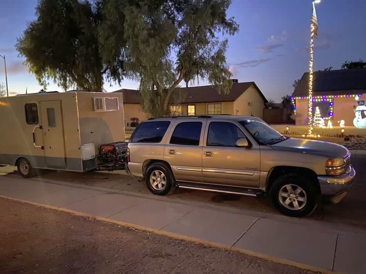 The Dirty Paws rig at a suburban curb at dusk: a gold SUV towing a white camper trailer converted into a mobile grooming unit.